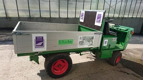 Ein grüner Traktor mit Anhänger steht vor einem Gewächshaus.