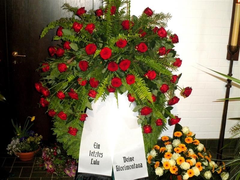 Ein Kranz aus roten Rosen mit einer weißen Schleife und der Aufschrift