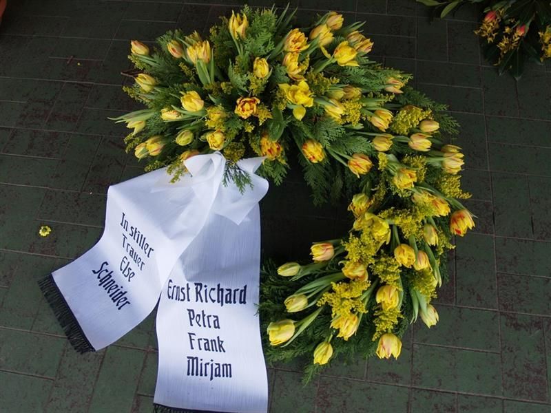 Ein Kranz aus gelben Blumen mit einem weißen Band, auf dem