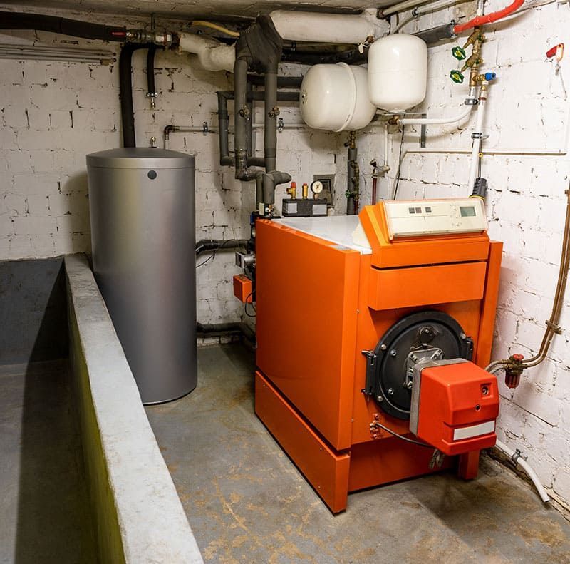 Chaudière orange dans une buanderie au sous-sol avec tuyaux, réservoirs et murs apparents