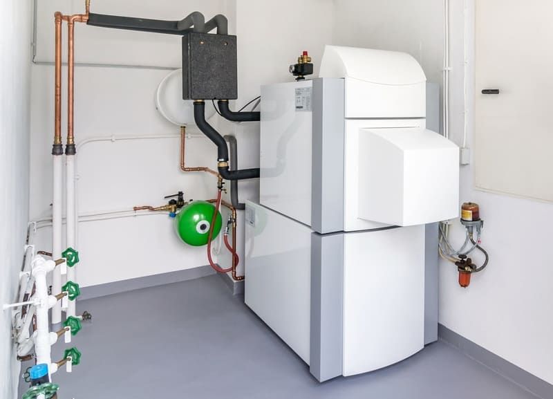 Unités de chauffage/climatisation blanches et tuyauterie dans un local technique propre, avec un vase d'expansion vert fixé au mur.