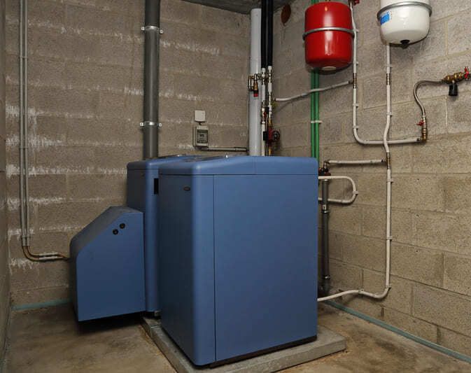 Chaudière bleue dans une buanderie au sous-sol, avec tuyaux apparents et vases d'expansion rouges et blancs.