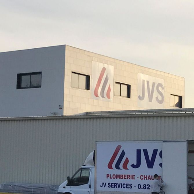 Bâtiment JVS avec logo et camionnette de livraison blanche garée devant au crépuscule