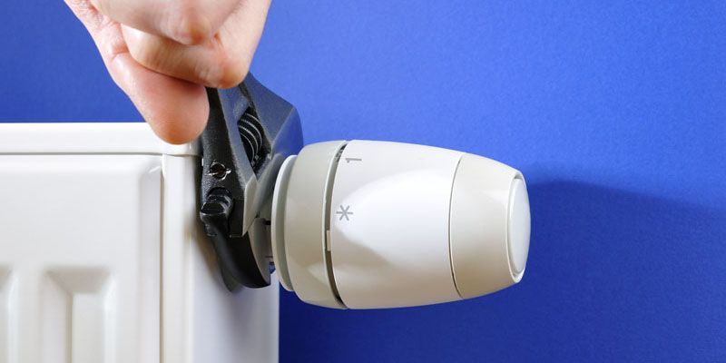 Serrage manuel d'un thermostat blanc sur un mur bleu, à côté d'un encadrement de porte blanc