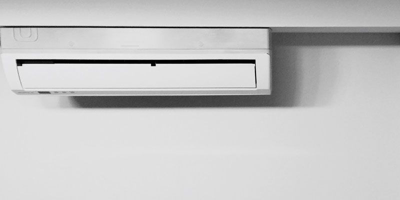 Climatiseur mural blanc sur un mur gris clair.