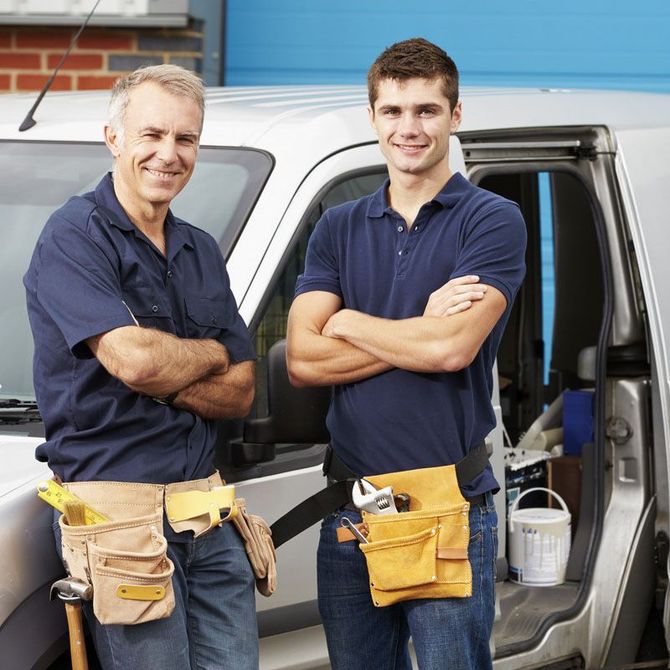 Deux ouvriers souriants, vêtus de chemises bleu marine et de ceintures à outils, se tiennent à côté d'une camionnette blanche.