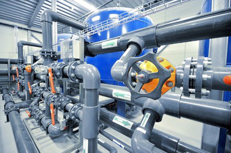 Tuyauterie industrielle avec tuyaux gris, vannes orange et machines bleues dans une salle des machines lumineuse