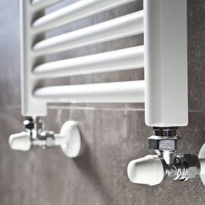Radiateur sèche-serviettes blanc avec robinetterie chromée contre un mur carrelé gris