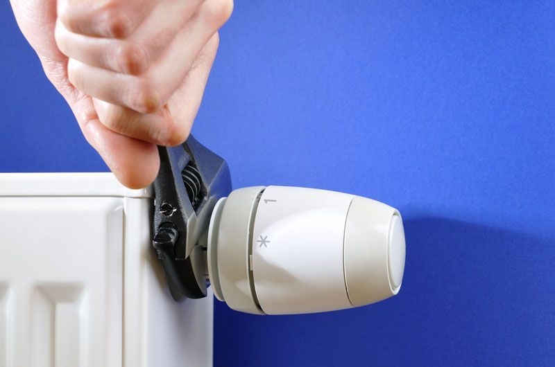 Serrage manuel d'un robinet de radiateur blanc à l'aide d'une clé contre un mur bleu