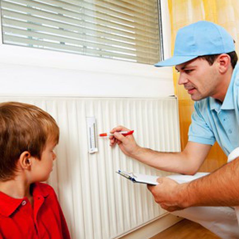 Un technicien vérifie un radiateur à l'aide d'un bloc-notes, sous le regard d'un enfant qui se trouve à proximité.