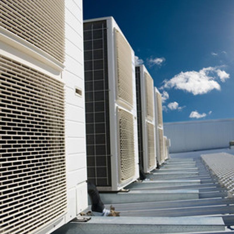 Rangée d'unités de climatisation sur le toit d'un immeuble blanc, sous un ciel d'un bleu éclatant.