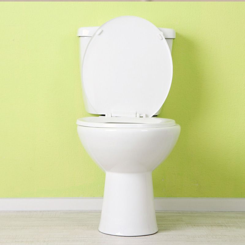 Toilettes blanches avec abattant et siège, contre un mur vert citron.