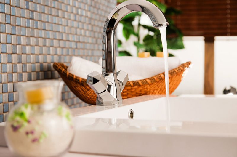 Robinet de cuisine chromé à côté d'un évier blanc avec panier en osier et crédence en mosaïque