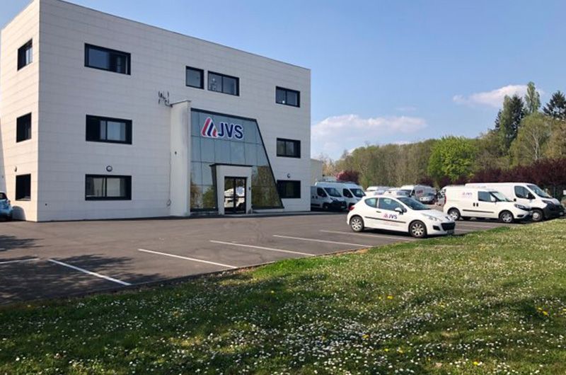 Immeuble de bureaux moderne avec voitures garées et pelouse au premier plan par une journée ensoleillée