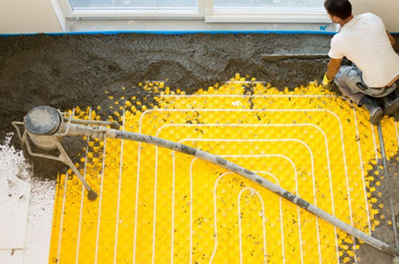 Ouvrier installant des tubes de chauffage au sol jaune vif dans une pièce en construction
