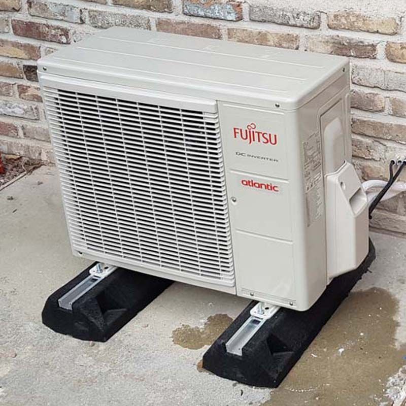 Unité de climatisation Fujitsu blanche sur supports noirs, à côté d'un mur de briques à l'extérieur