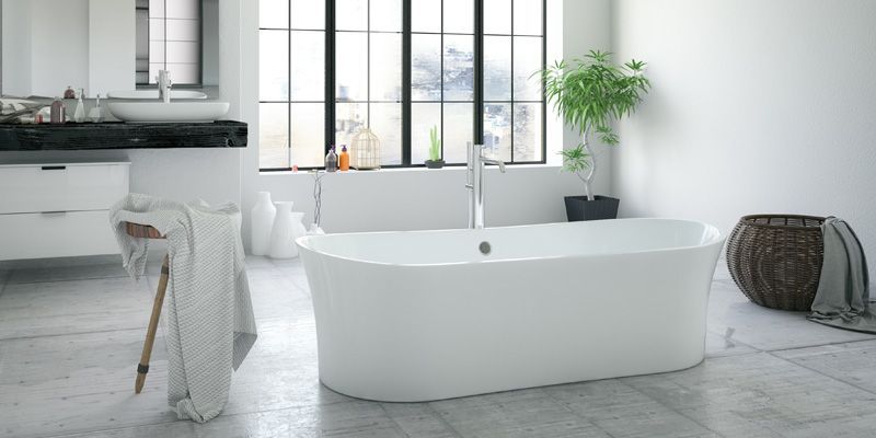 Salle de bains lumineuse et minimaliste avec baignoire blanche sur pieds, baies vitrées et plante en pot.