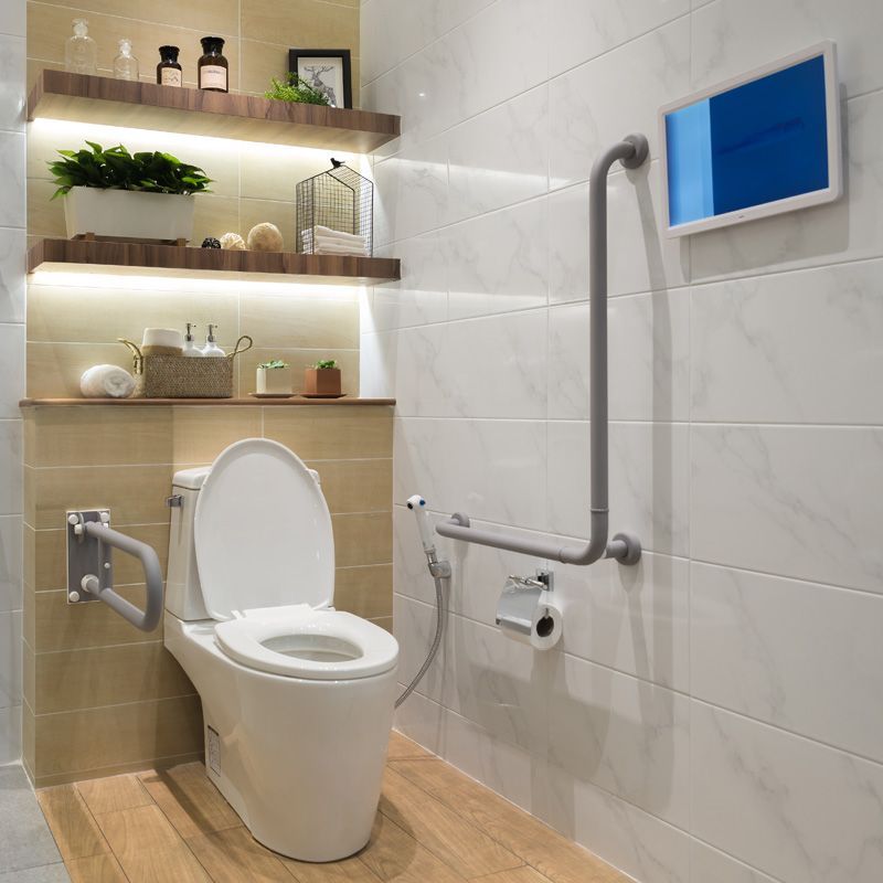 Salle de bain accessible avec toilettes blanches, barres d'appui, étagères et murs carrelés.