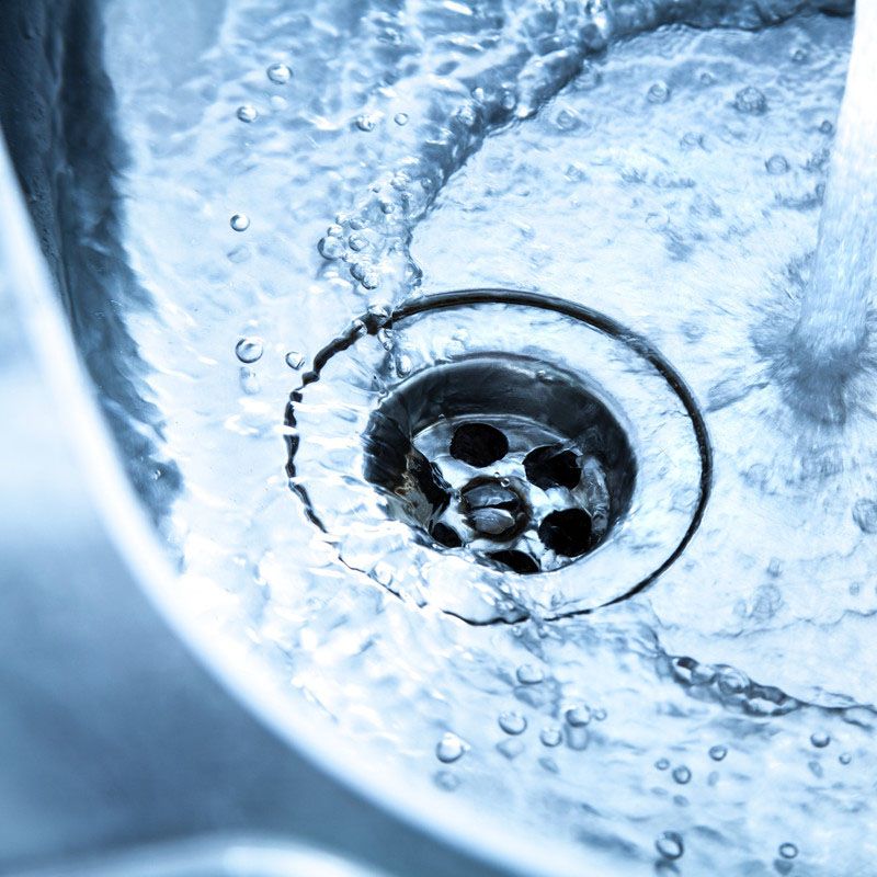 Gros plan sur une bonde métallique entourée d'eau tourbillonnante dans un évier aux reflets bleutés