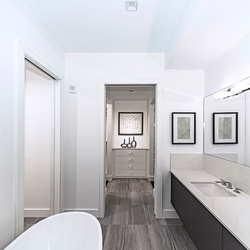 Salle de bains moderne blanche avec un long meuble-lavabo, un miroir et une porte donnant sur un petit dressing.