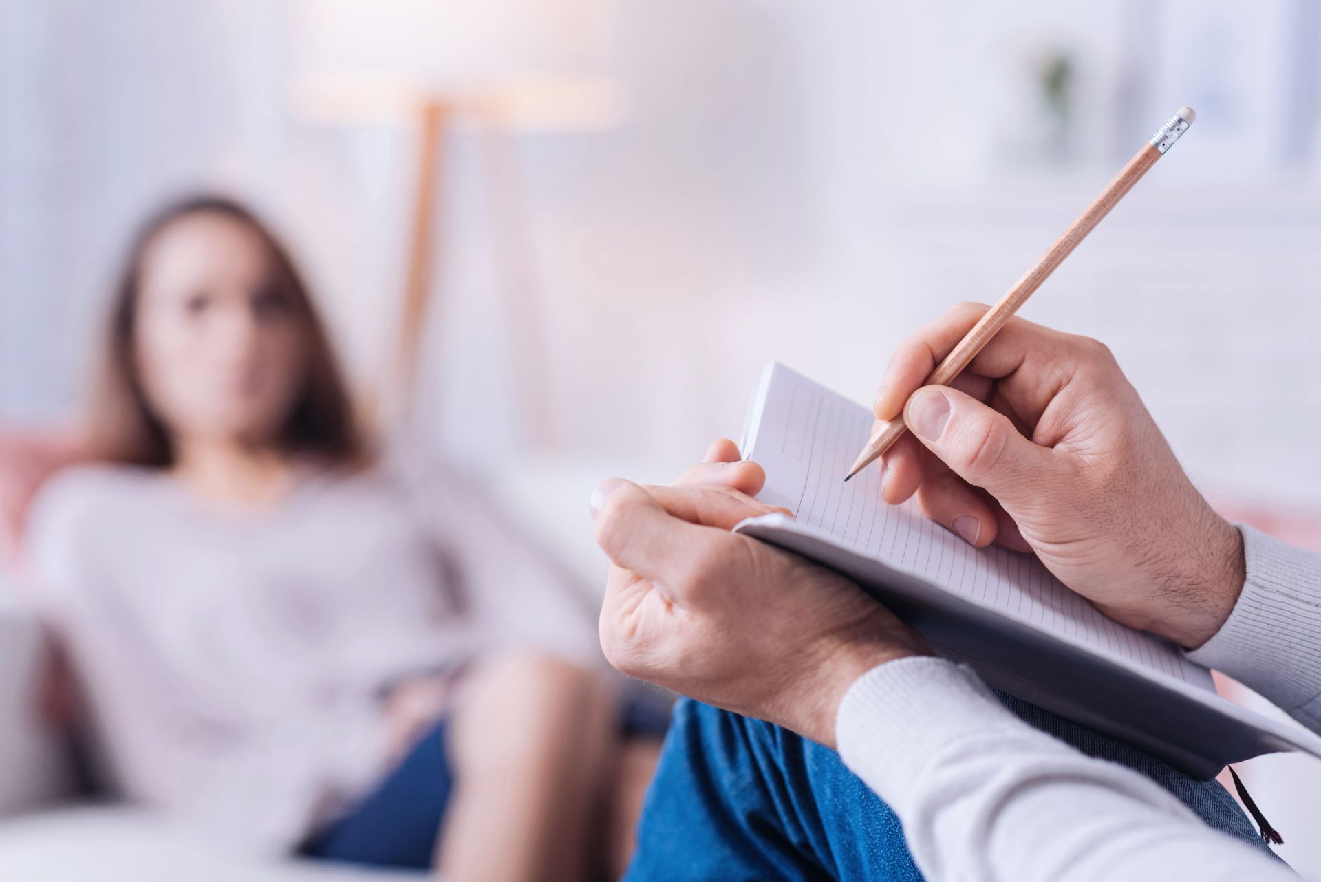 Une thérapeute prend des notes pendant qu'un client assis parle dans une salle de consultation à l'éclairage tamisé.