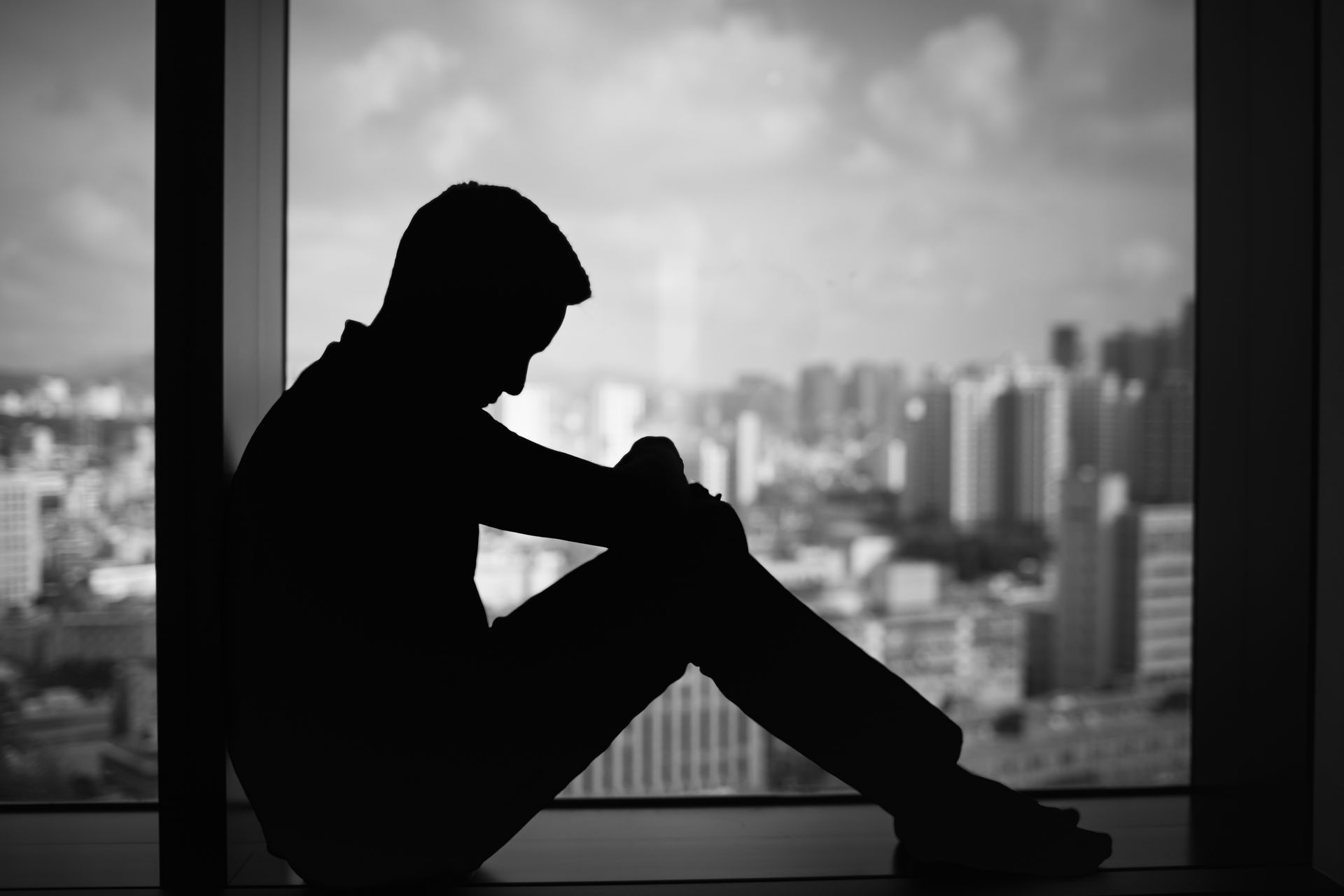 Silhouette d'une personne assise près d'une fenêtre, donnant sur une vue urbaine floue.
