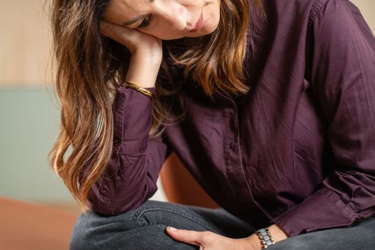 Une femme assise sur un canapé, la tête appuyée sur sa main, affiche une expression fatiguée ou pensive.