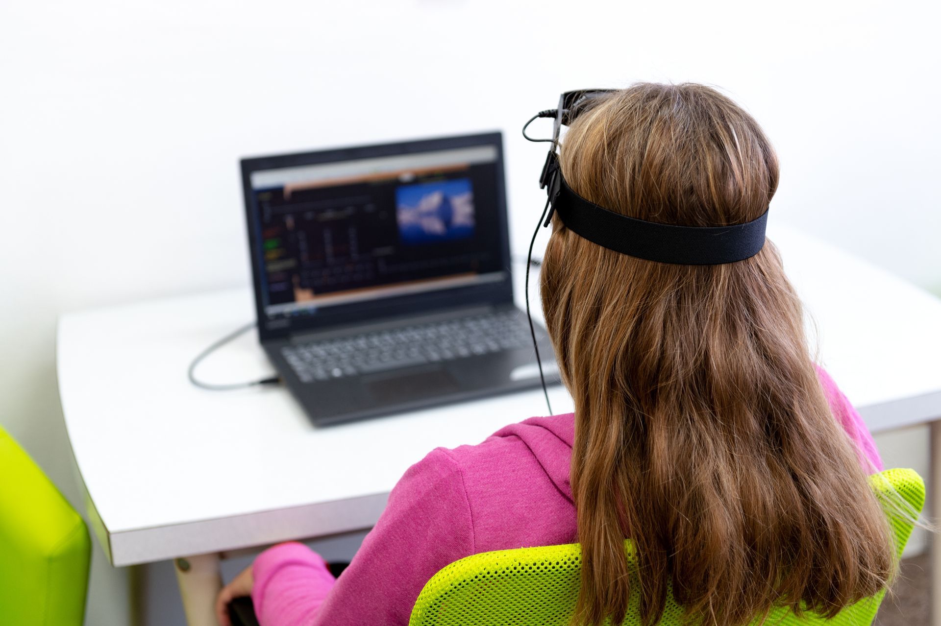Une personne portant un casque est assise devant un ordinateur portable à un bureau blanc.