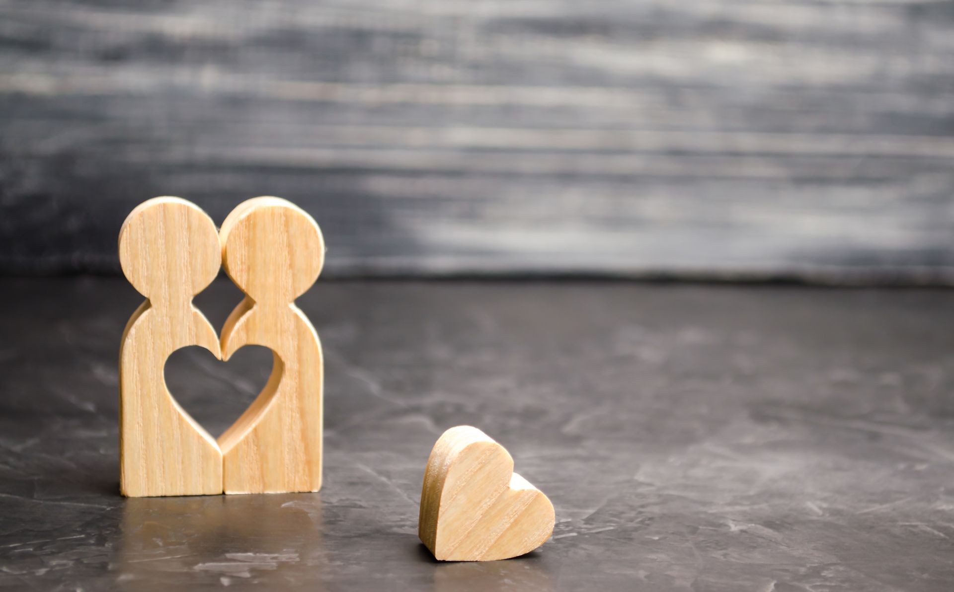 Deux décorations en bois sur une surface en bois gris, l'une est composée de 2 silhouettes en forme de cœur et l'autre est un cœur.