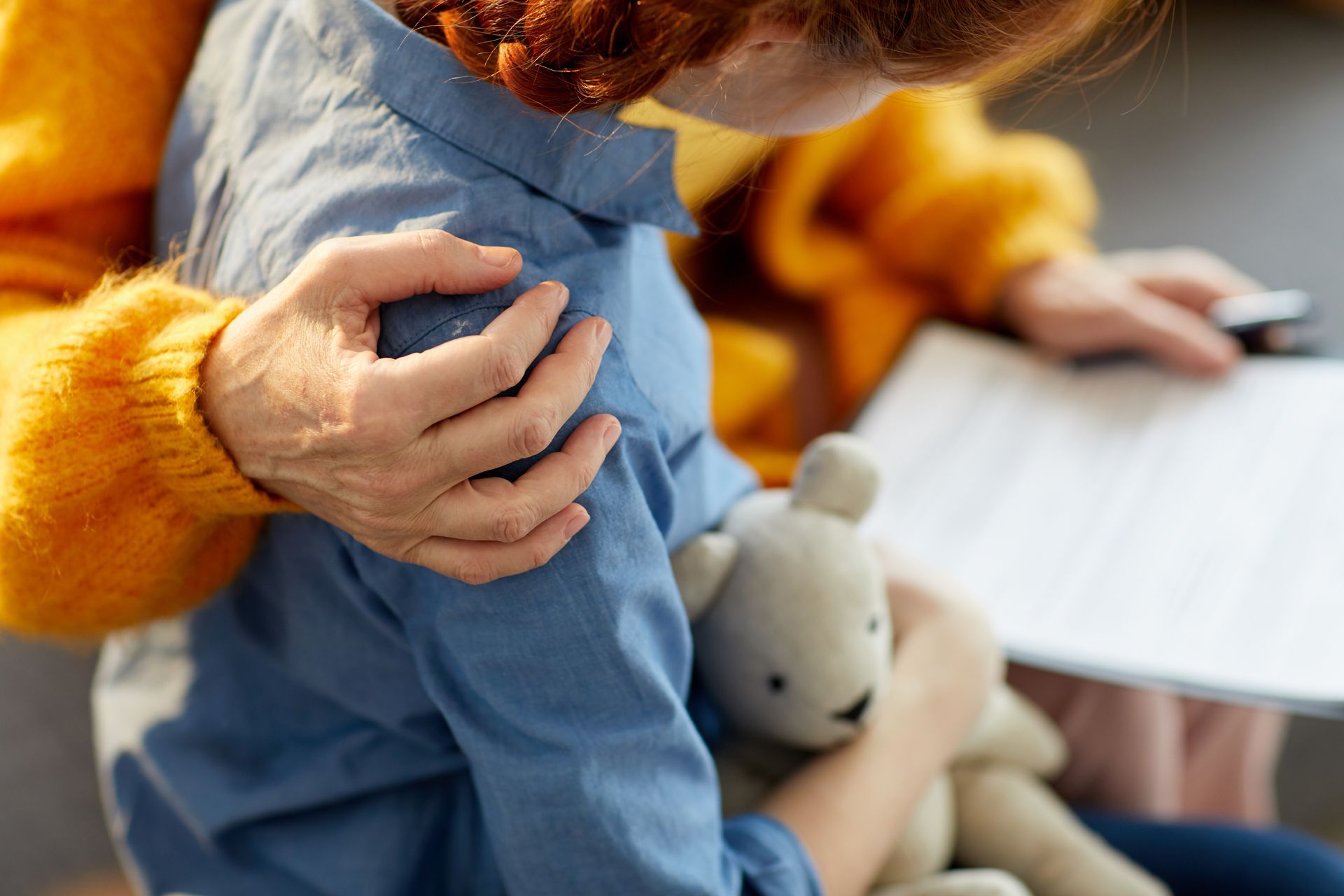 Un adulte tenant par l'épaule un enfant vêtu d'une tenue bleue, avec un petit lapin en peluche dans les bras.