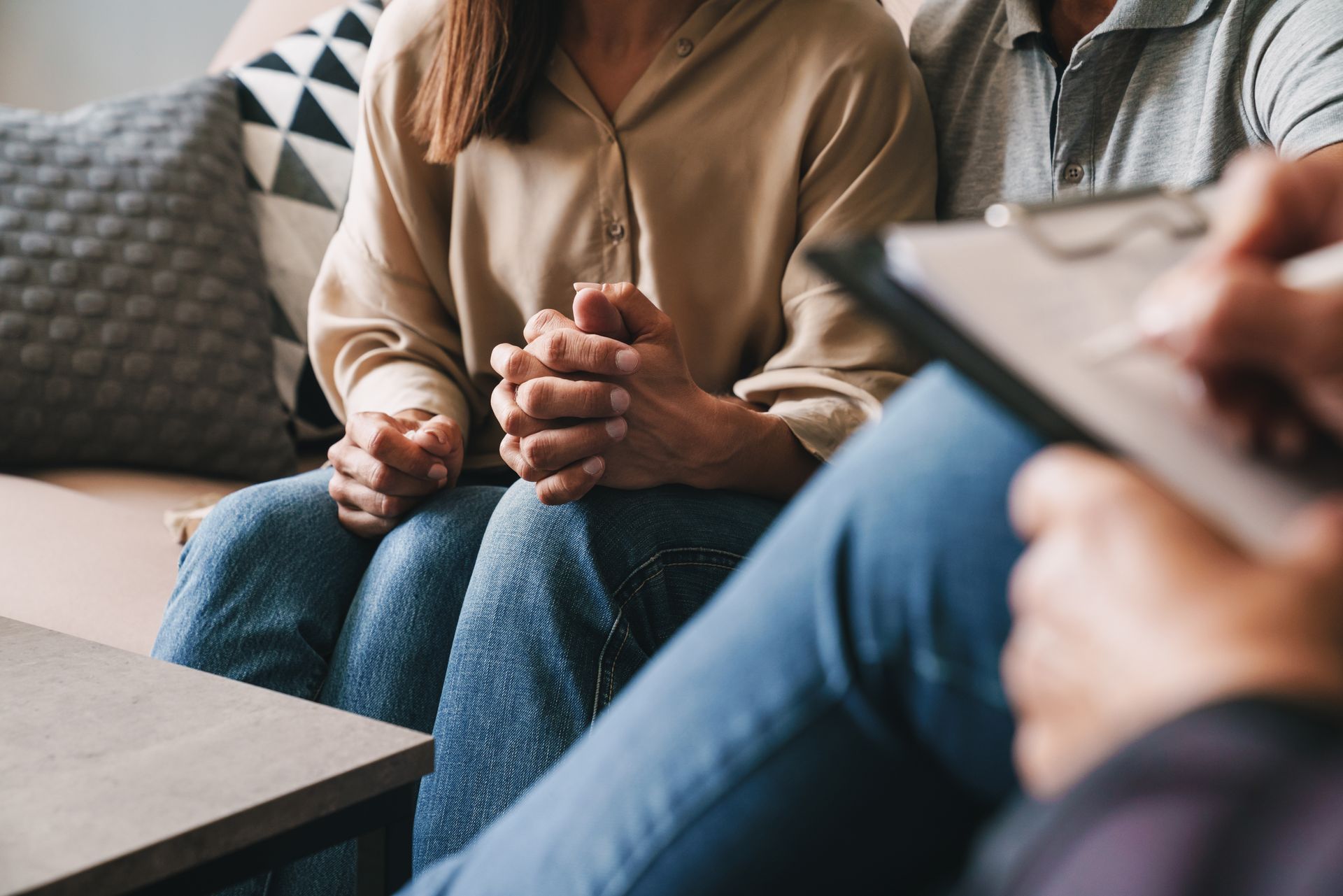 Trois personnes assises dans un salon, l'une tenant une tablette tandis que les autres discutent en se tenant la main.
