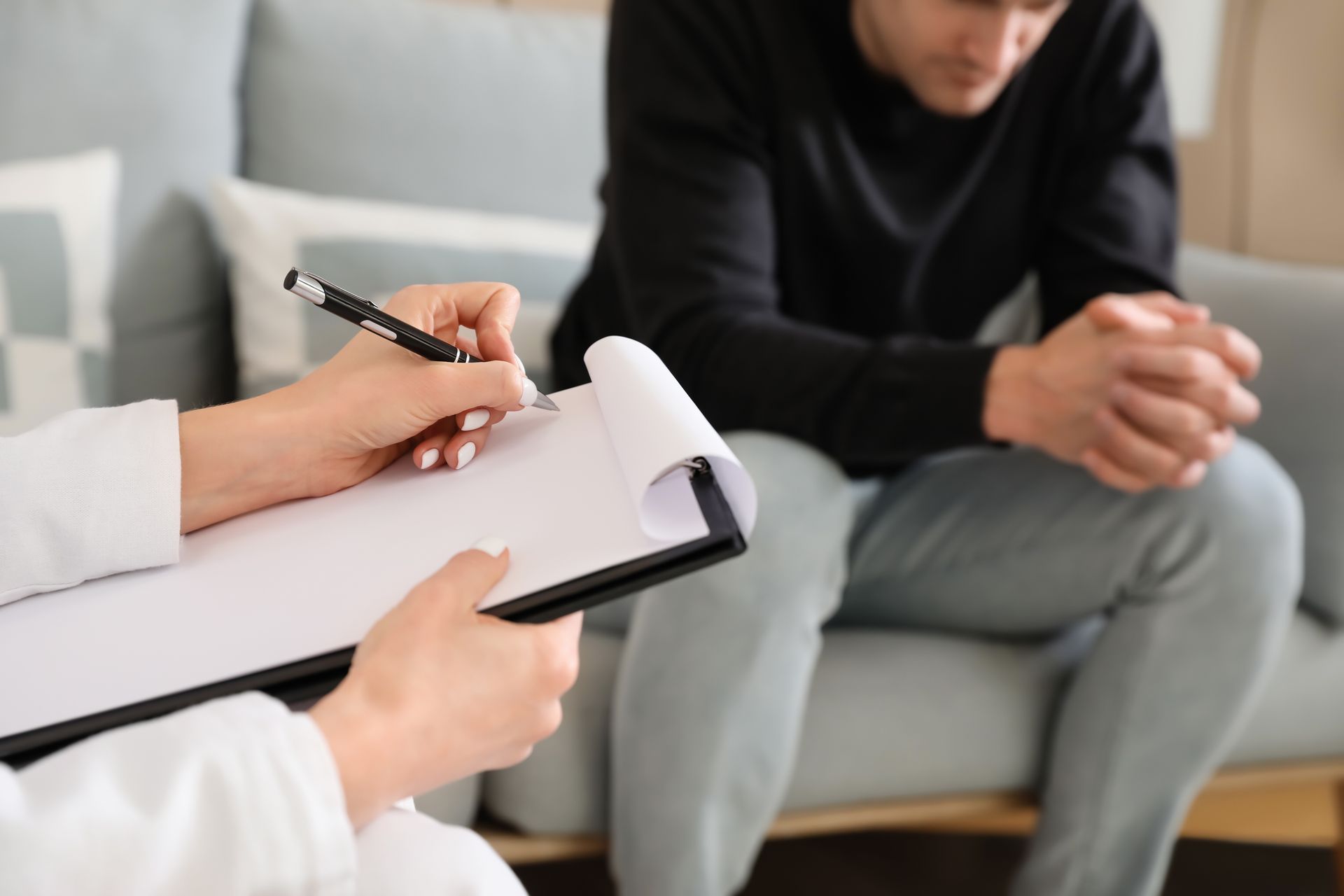 La thérapeute prend des notes pendant une consultation avec un patient assis sur un canapé.