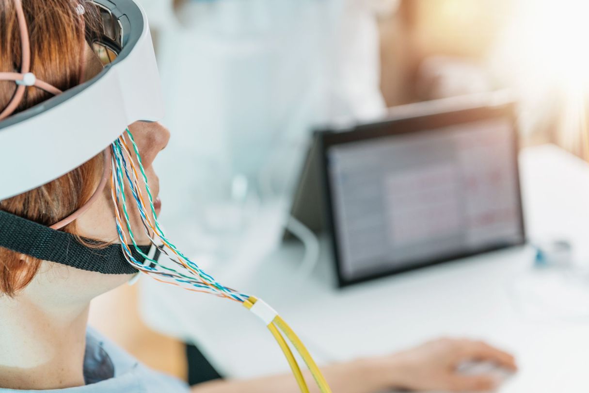 Une personne portant un casque EEG devant un ordinateur portable dans une pièce lumineuse.