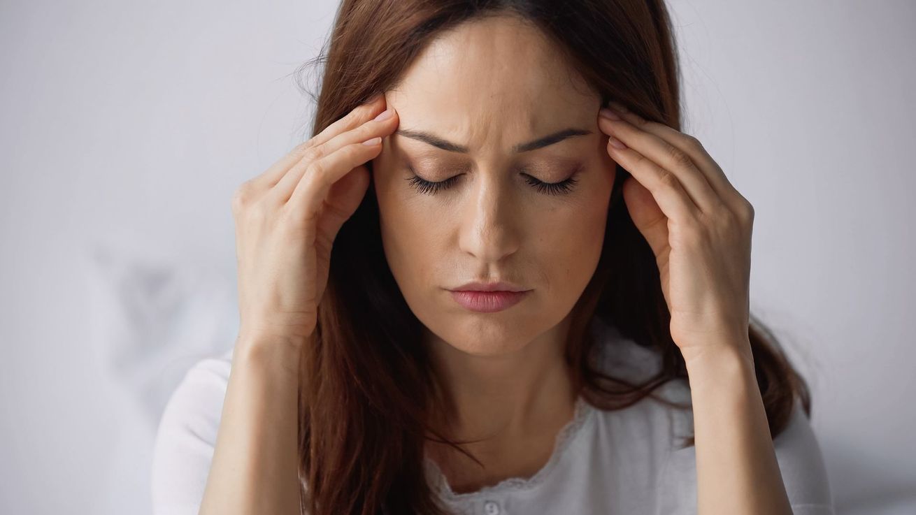 Une femme se presse les tempes avec une expression de douleur, suggérant un mal de tête ou du stress.