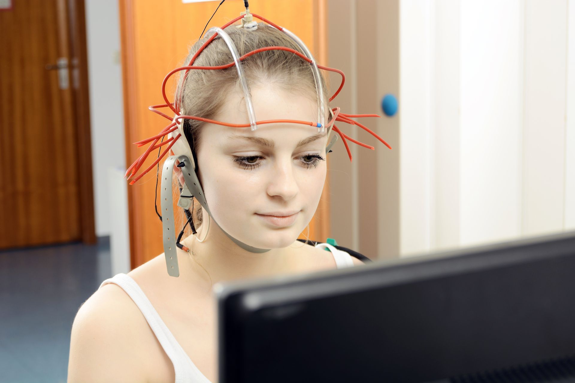 Une personne portant un casque EEG regarde un écran d'ordinateur dans une pièce lumineuse.