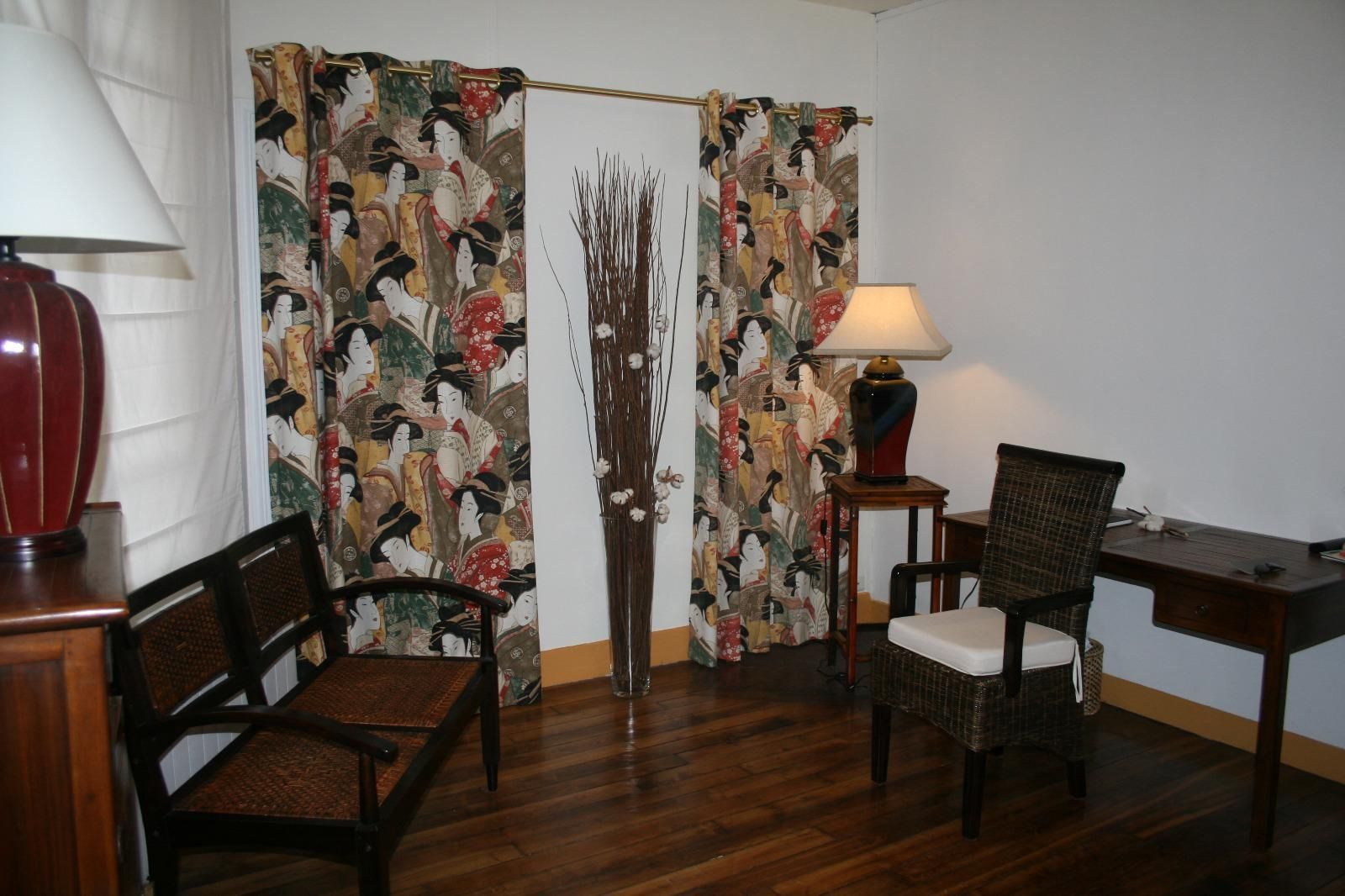 Salon avec des rideaux à motifs japonais, chaise en bois, lampe de table et meubles en bois foncé sur un sol en parquet.