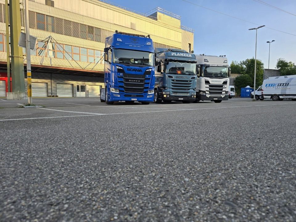 Auf einem Parkplatz vor einem Gebäude steht eine Reihe von Lastwagen.