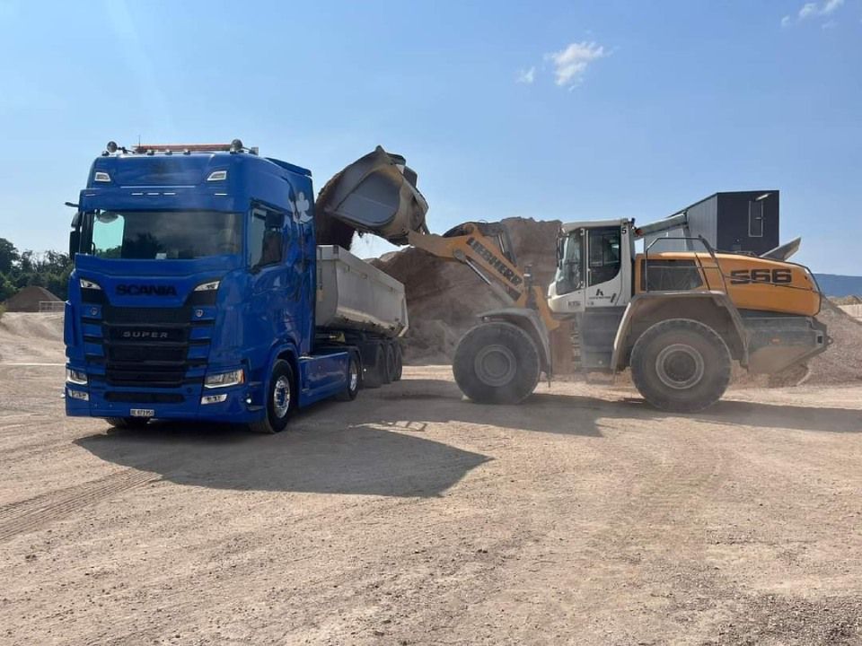 Ein blauer Lastwagen wird von einem gelben Bulldozer mit Erde beladen.