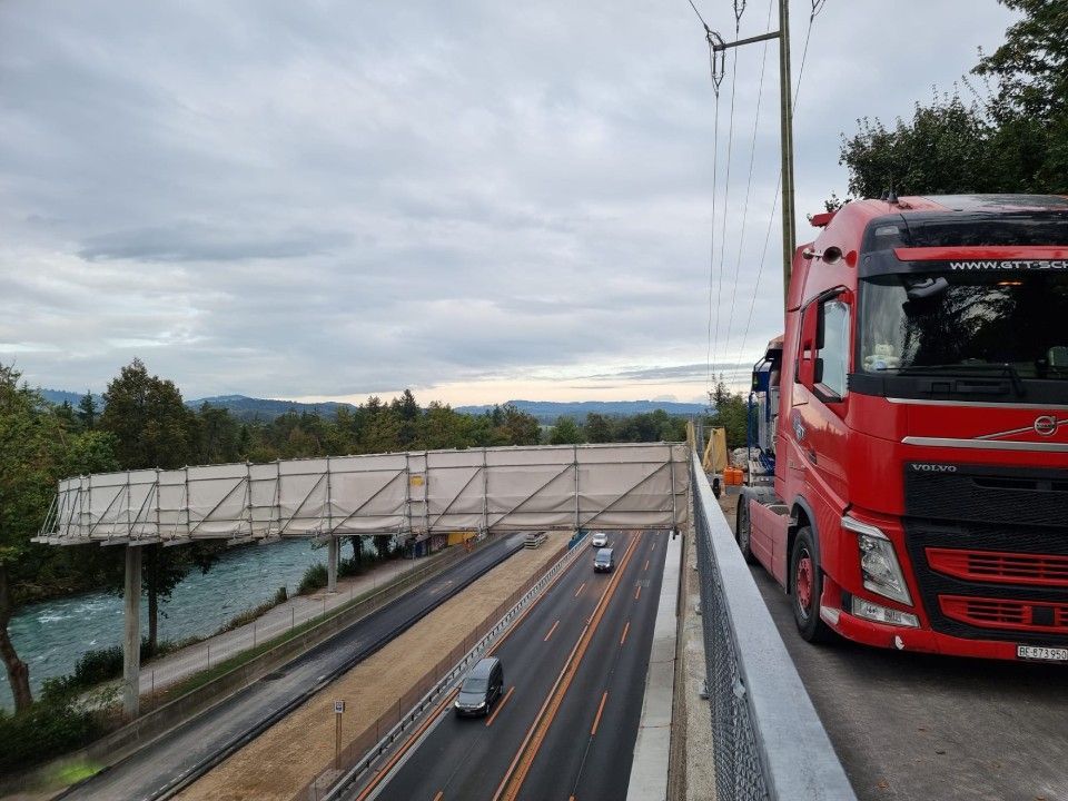 Ein roter Lastwagen fährt auf einer Autobahn neben einer Brücke