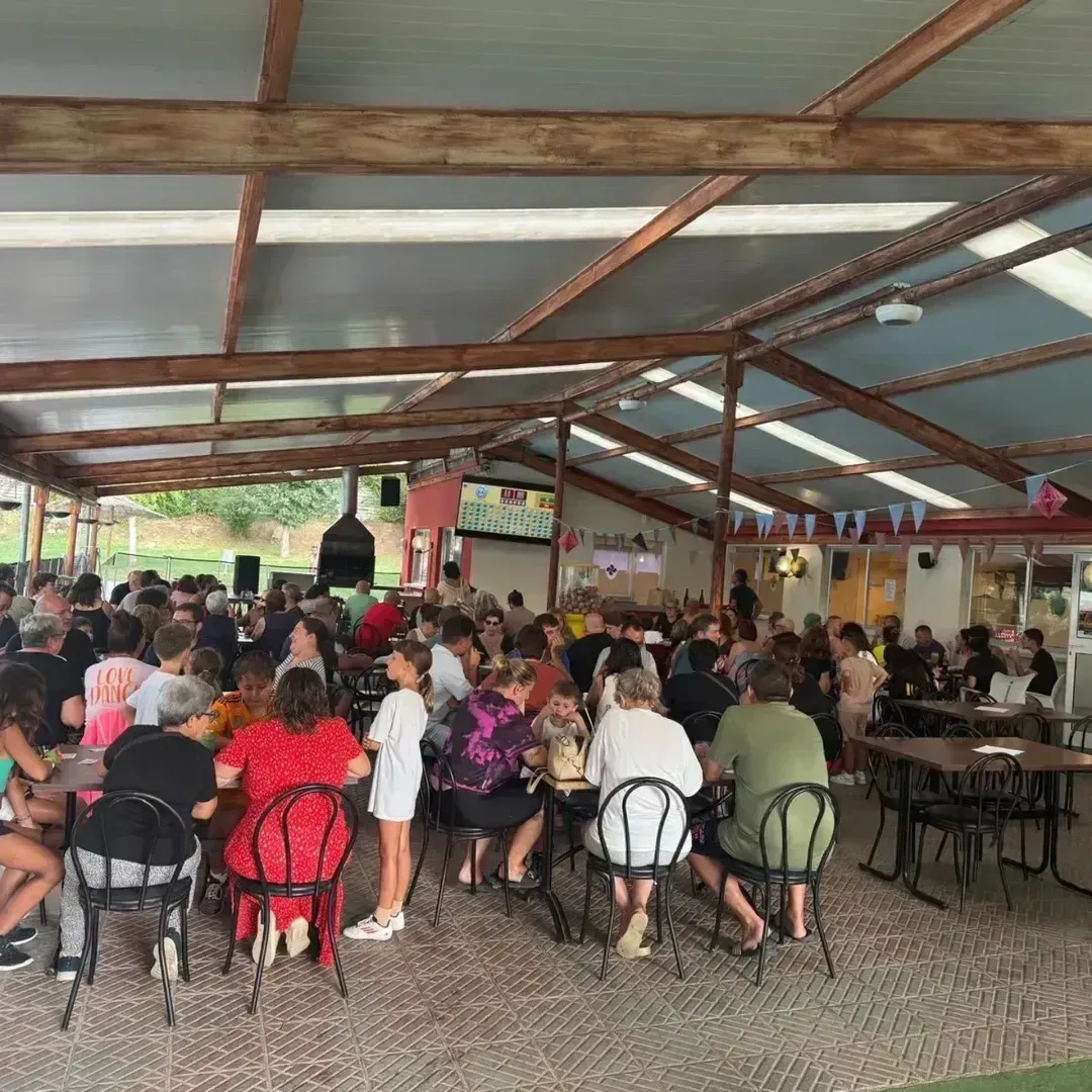 Gran reunión al aire libre bajo techo. La gente, sentada y de pie, socializa.