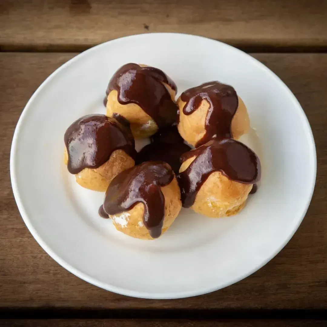Profiteroles, pasteles rellenos de crema, con ganache de chocolate en un plato blanco