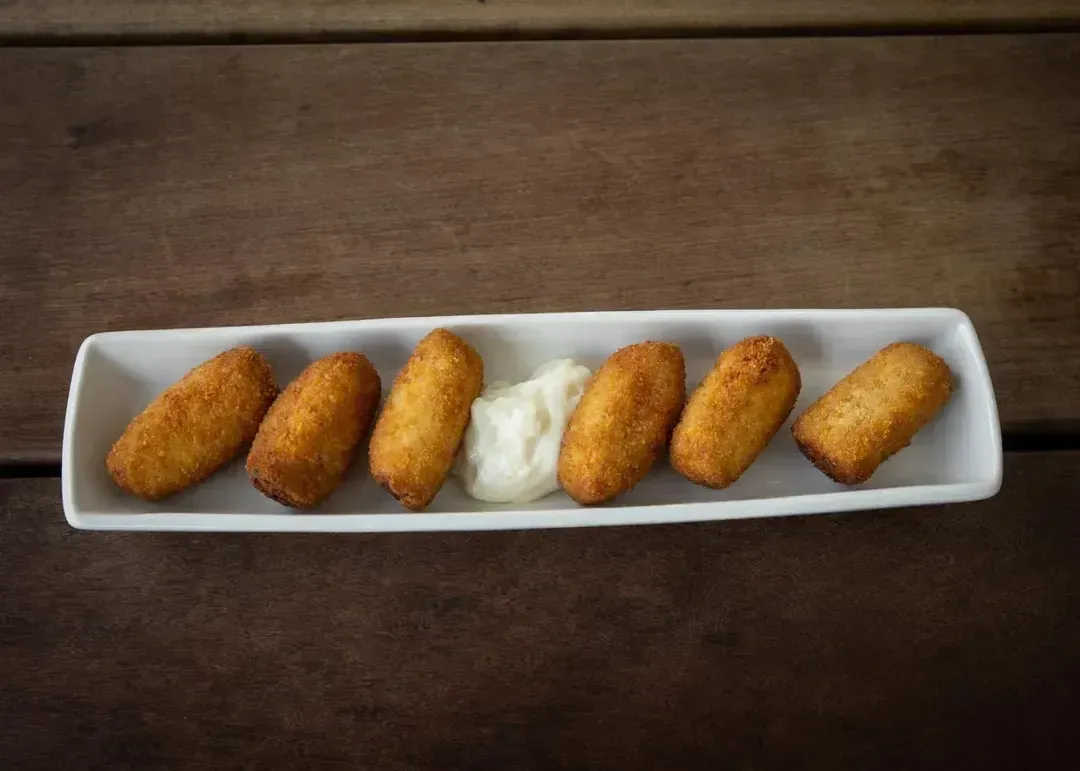 Seis croquetas doradas y una cucharada de salsa blanca sobre un plato rectangular blanco