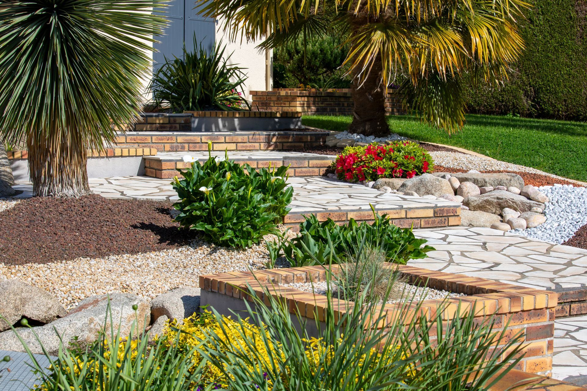 Jardin désertique aménagé avec allées de pierre, palmiers et arbustes fleuris.