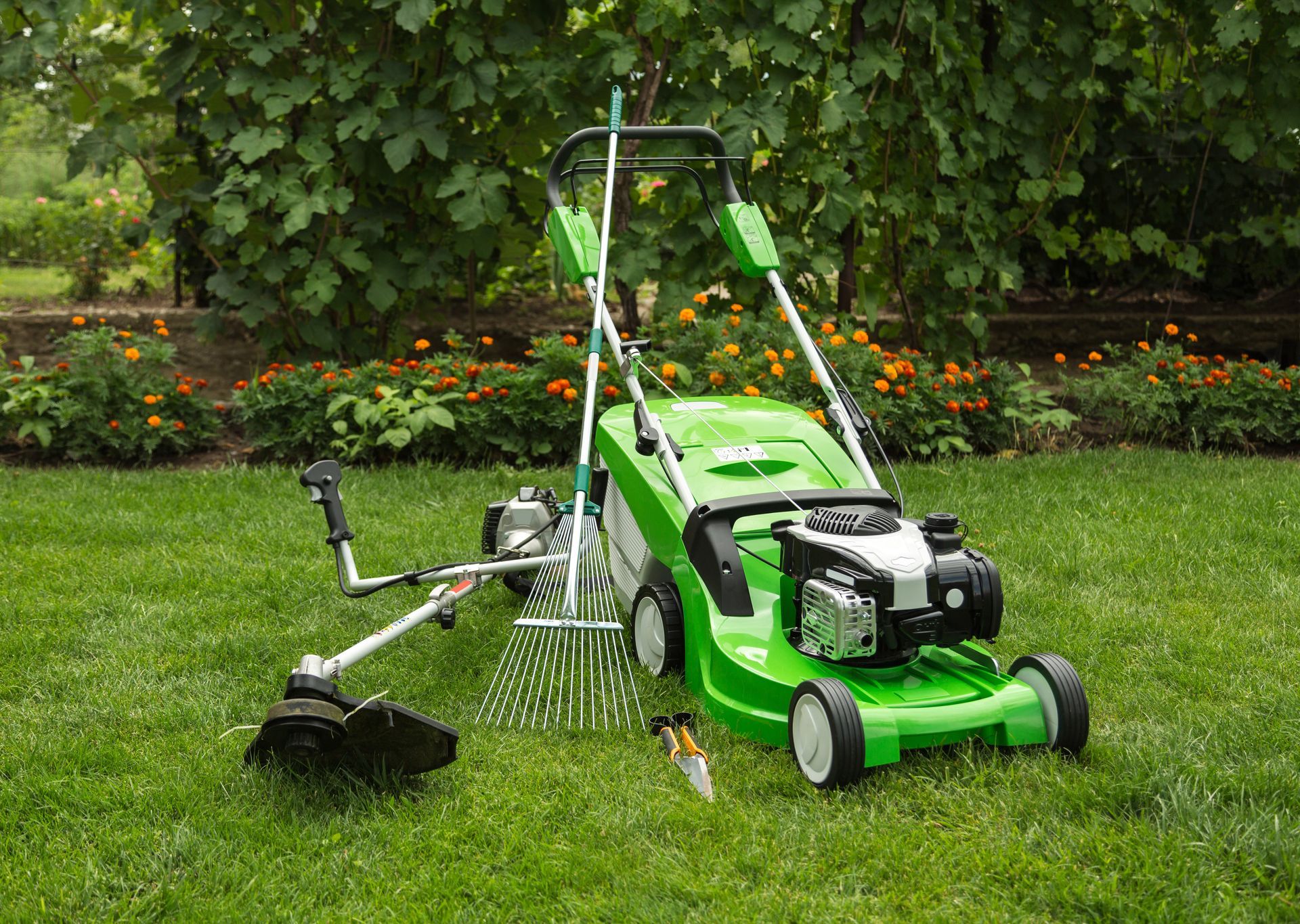 Tondeuse à gazon verte avec coupe-bordures et taille-haies sur une pelouse dans un jardin