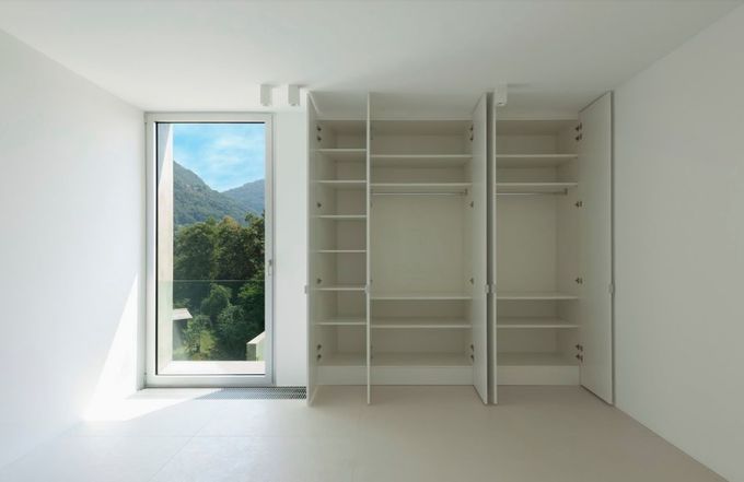 Habitación luminosa y vacía con armarios empotrados y una ventana alta con vistas a la vegetación y las montañas.