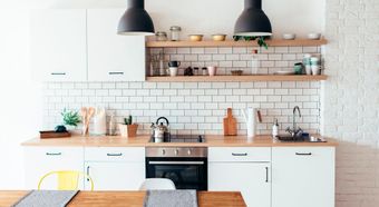 Cocina moderna y luminosa con armarios blancos, encimeras de madera, azulejos tipo metro y lámparas colgantes negras.