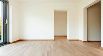 Habitación moderna vacía con suelos de madera clara, paredes blancas y grandes ventanas y puertas.
