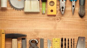 Diversas herramientas manuales dispuestas sobre un banco de trabajo de madera, entre las que se incluyen alicates, llave inglesa, martillo, sierra y juego de destornilladores.