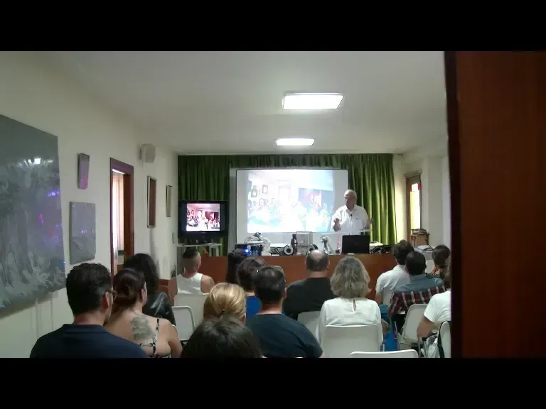Un hombre da una conferencia. El público está sentado frente a una pantalla.