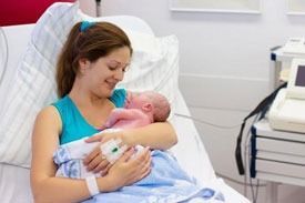 Una madre en una cama de hospital sostiene a su bebé recién nacido, sonriendo.